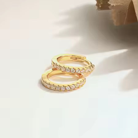 Gold diamond hoop earrings with embedded stones on a light background