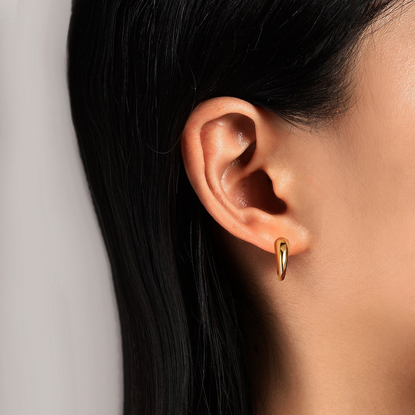 Close-up of an ear wearing a Gold Dome hoop earrings with a neutral background