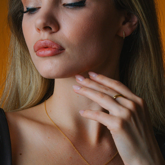 Close-up of a woman wearing a gold necklace and ring & daimond hoop with a blurred background