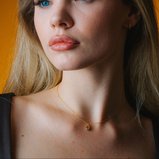 Close-up of a woman wearing a gold necklace with a small diamond pendant against an orange background