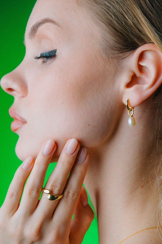 Close-up of a woman's face with gold earrings and Duo Dome Gold ring against a green background