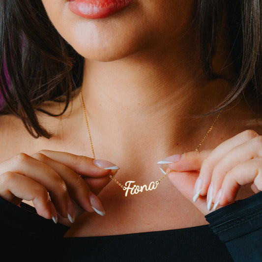 Woman wearing a gold necklace with 'Fiona' on it, close-up of neck and hands.