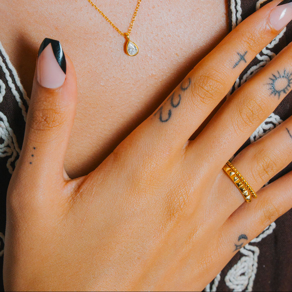 Close-up of a person wearing a gold necklace and Gold beaded ring, band stackable with a blurred background