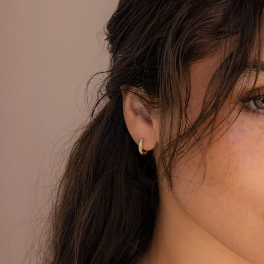 Close-up of a woman wearing Gold Huggies hoop earrings with opal inlay against a neutral background