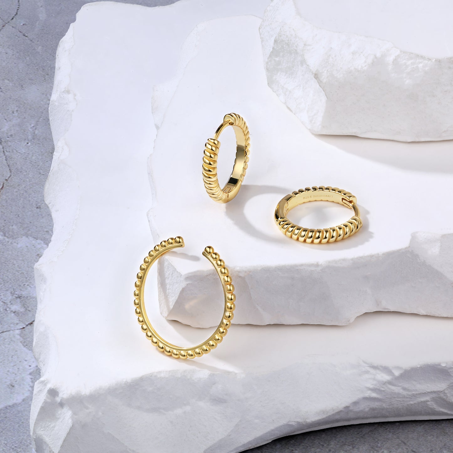 18k Gold twist huggee hoop earrings & Gold beaded ring, band stackable on a textured white surface