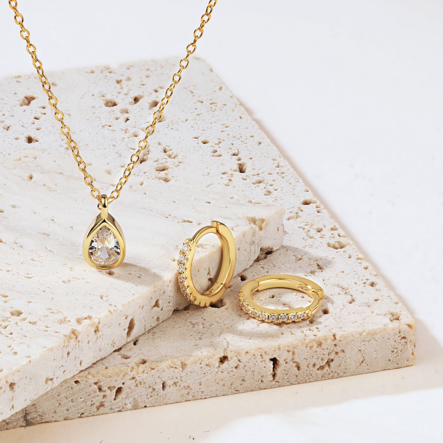 Gold diamond necklace, earrings, set on a textured stone surface