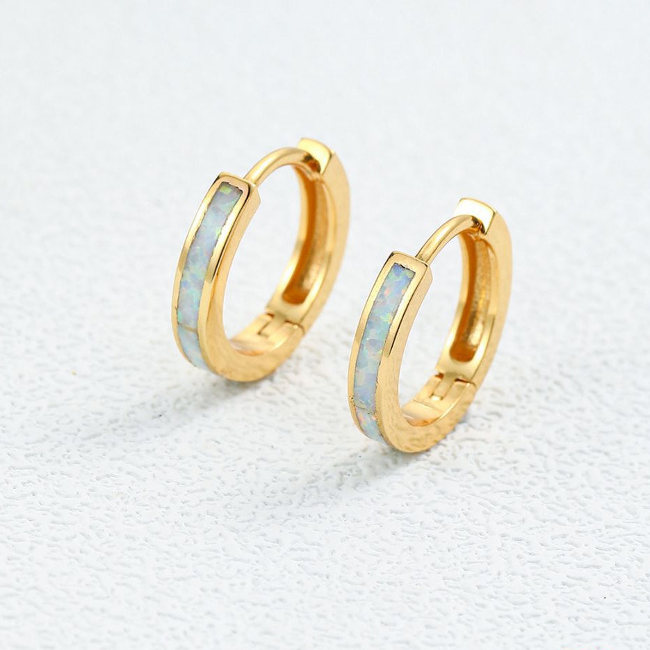 Gold Huggies hoop earrings with opal inlay  with light blue interior on a textured white background