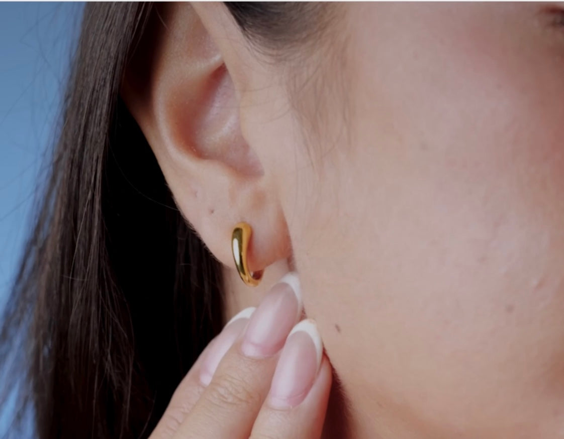 Close-up of a person wearing a Gold Dome hoop earrings with a blurred background