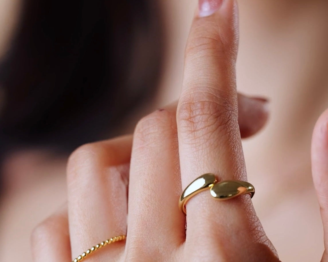 Close-up of a hand wearing a Duo Dome Gold ring with a blurred background