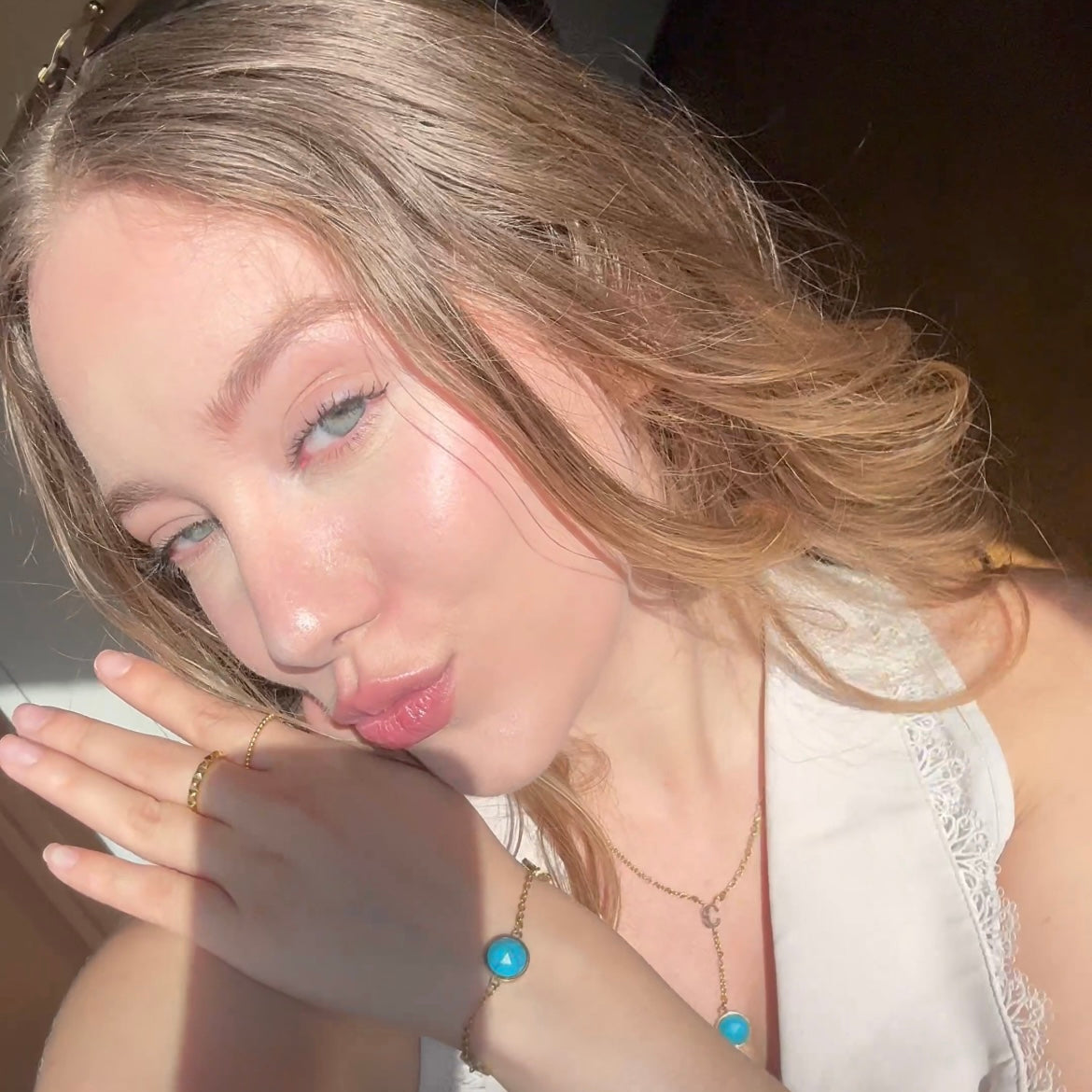 Woman with blonde hair and blue eyes, wearing a white top and turquoise bracelet & necklace
