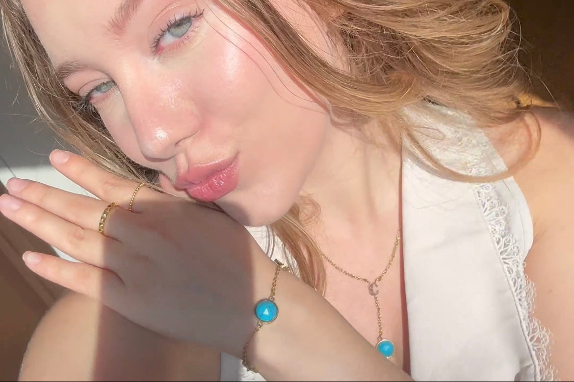 Woman with blonde hair and blue eyes, wearing a white top and turquoise bracelet & necklace