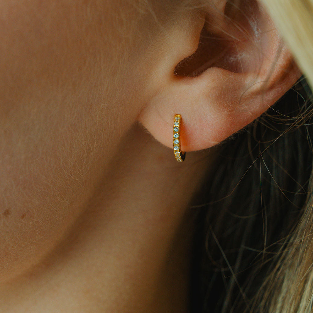 Close-up of an ear wearing a diamond gold hoop earring with small stones.