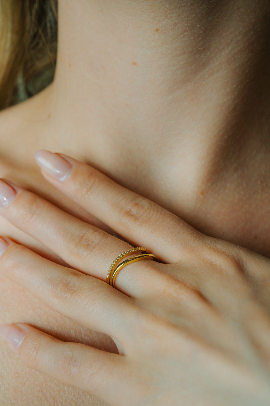Close-up of a hand wearing a Duo Wave Stacking gold Ring Set with a blurred background