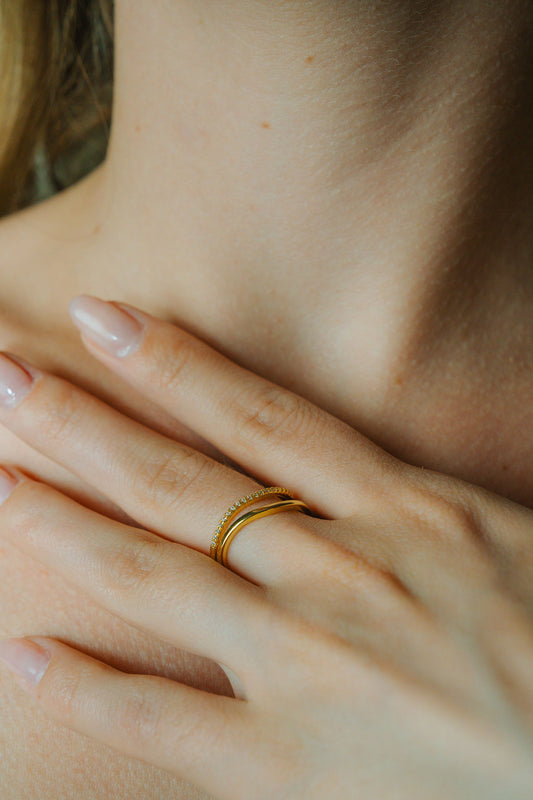 Close-up of a hand wearing a Duo Wave Stacking gold Ring Set with a blurred background
