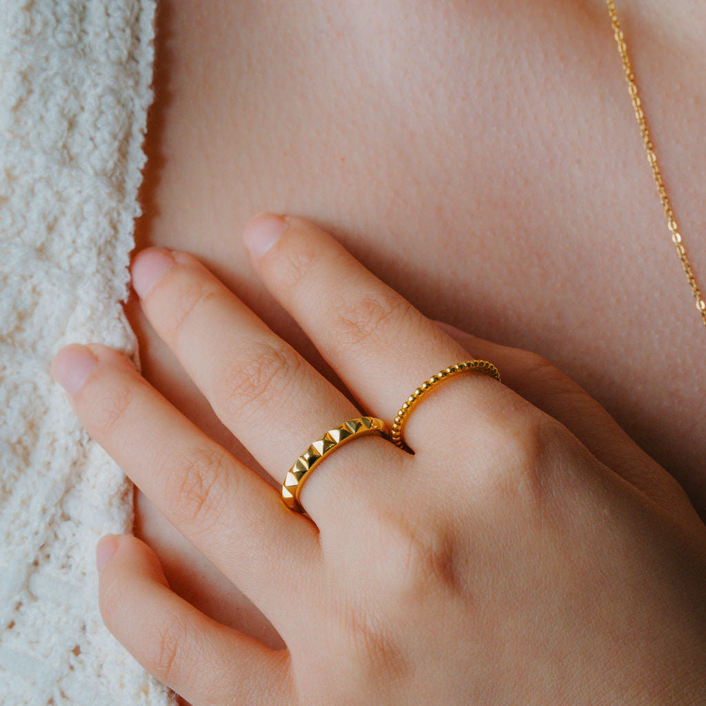 Close-up of a hand wearing a Gold beaded ring, a stackable band  & a gold Pyramid ring.