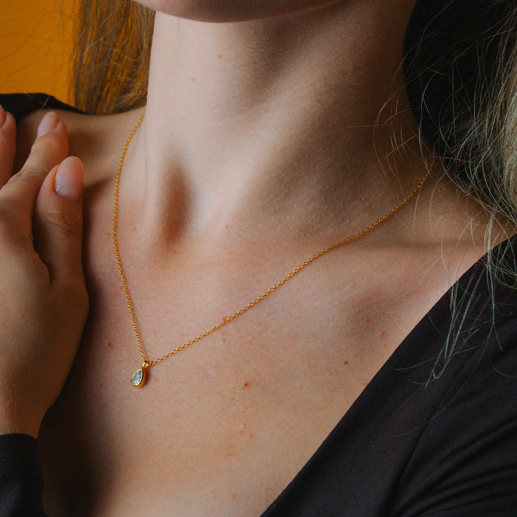 Close-up of a person wearing a gold necklace with a small diamond pendant.