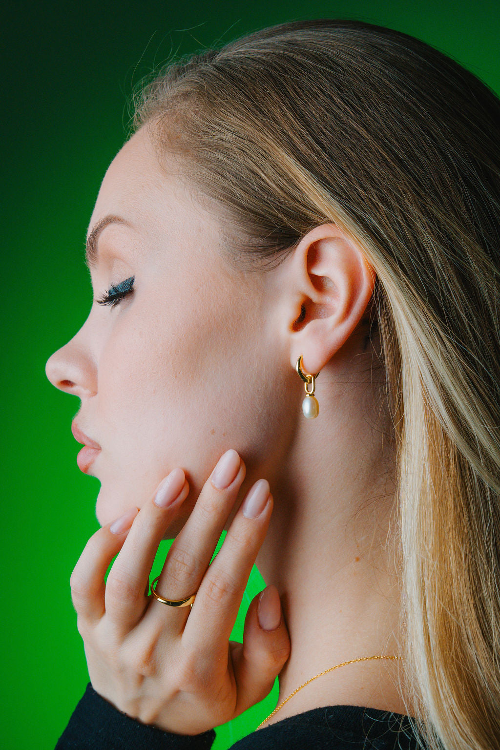 Close-up of a woman wearing a gold pearl earring with a green background