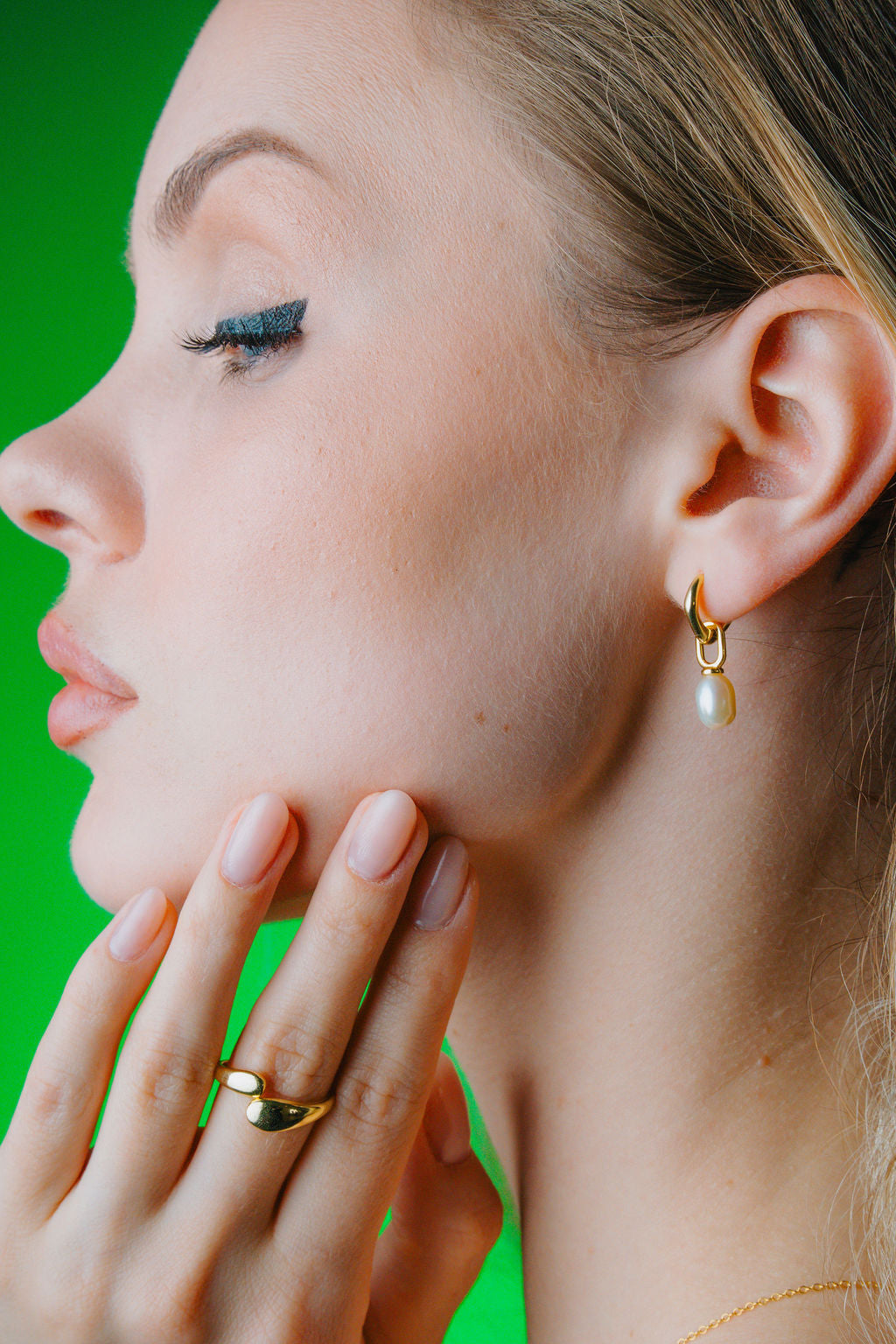 Close-up of a woman wearing a pearl  gold earring and ring against a green background