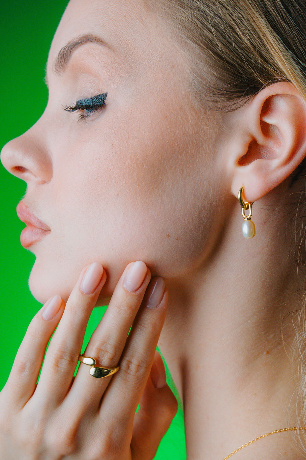 Close-up of a woman's face with gold earrings and Duo Dome Gold ring against a green background