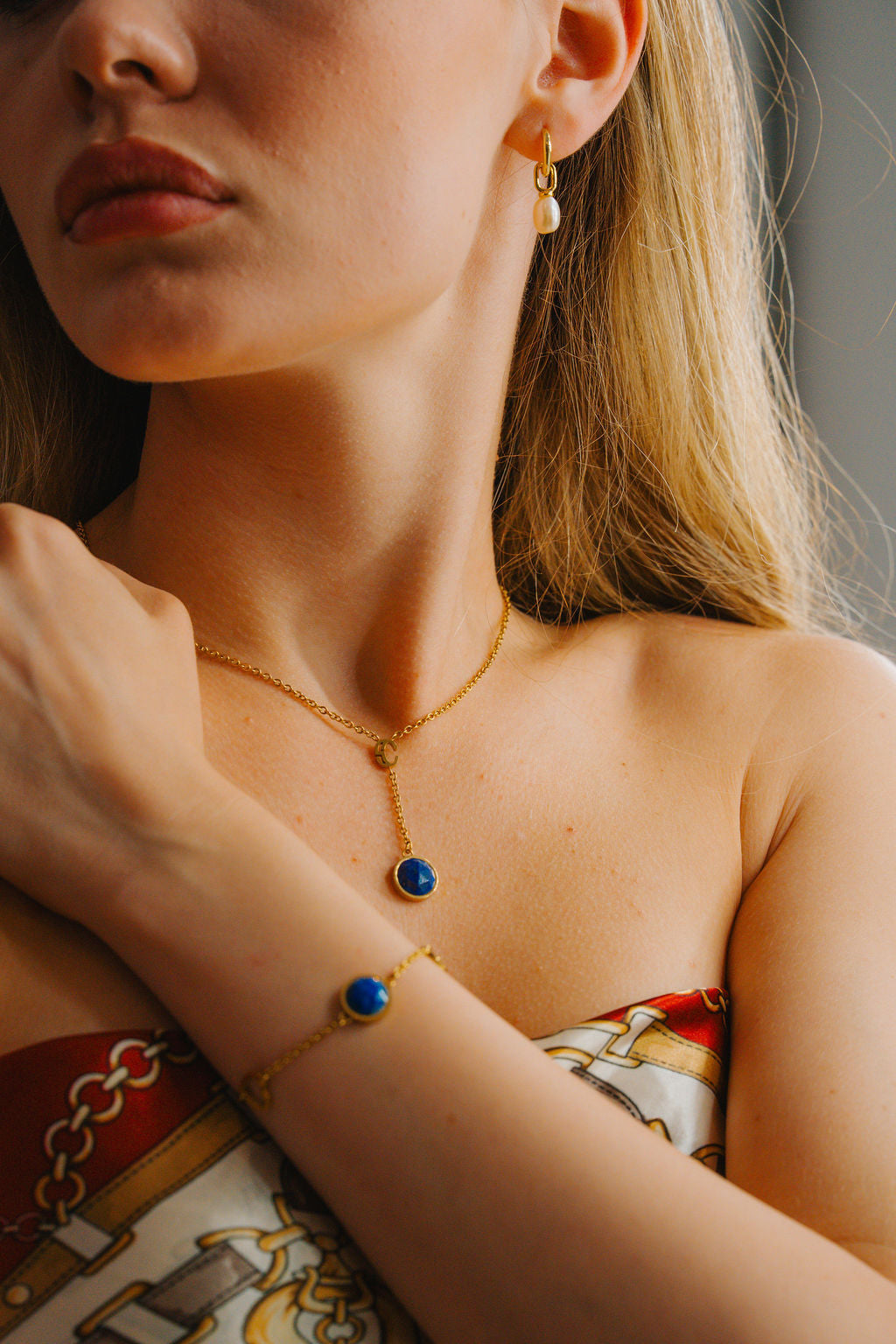 Close-up of a person wearing gold  lapis lazuli jewelry with a neutral background