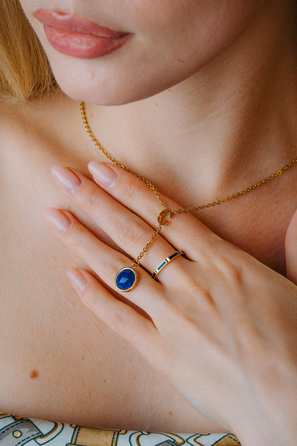 Close-up of a person wearing gold jewelry with a blue  lapis lazuli  gemstone on a neutral background