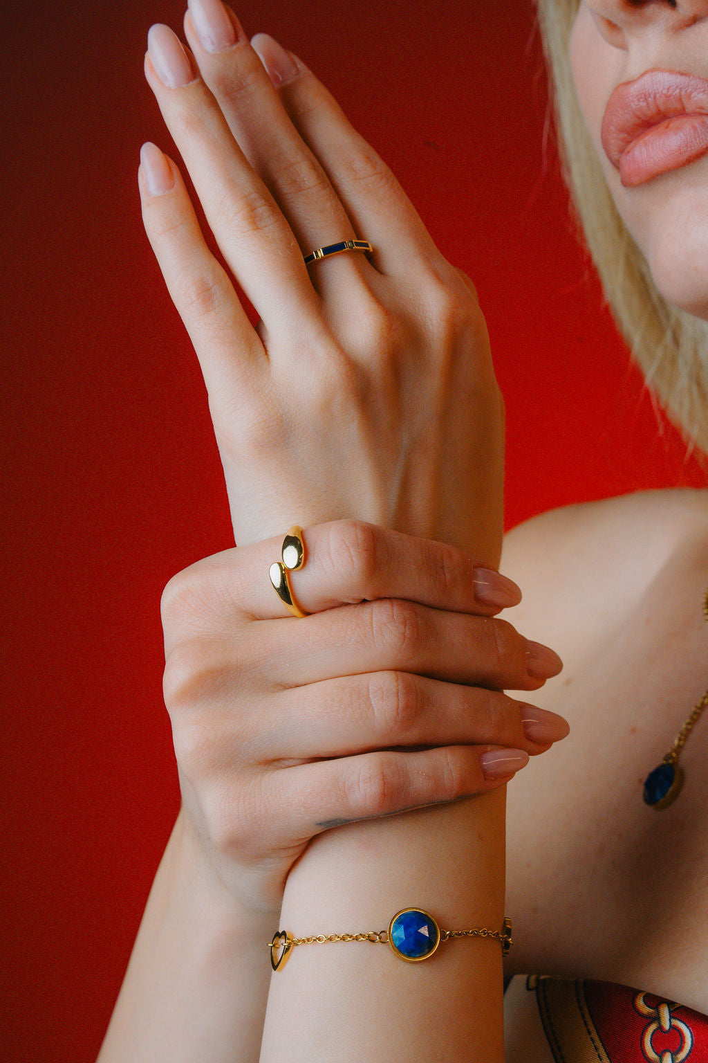 Close-up of a person's hand and arm with multiple rings and a lapiz lazuli bracelet against a red background