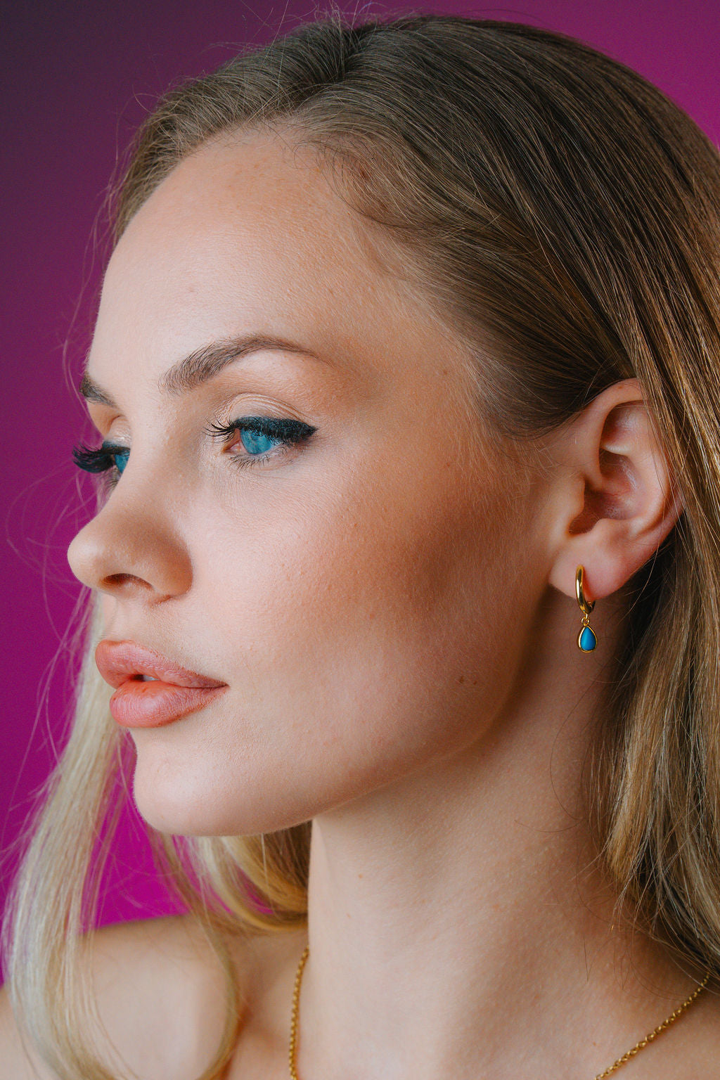 Close-up of a woman wearing gold earrings with blue stones against a purple background