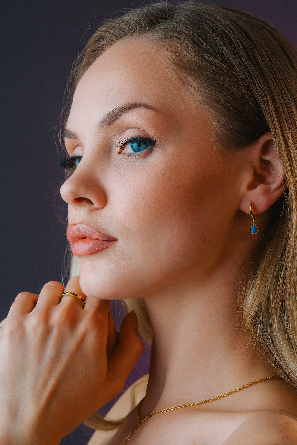 Close-up of a woman with blue eyes and blonde hair, wearing earrings and a necklace.