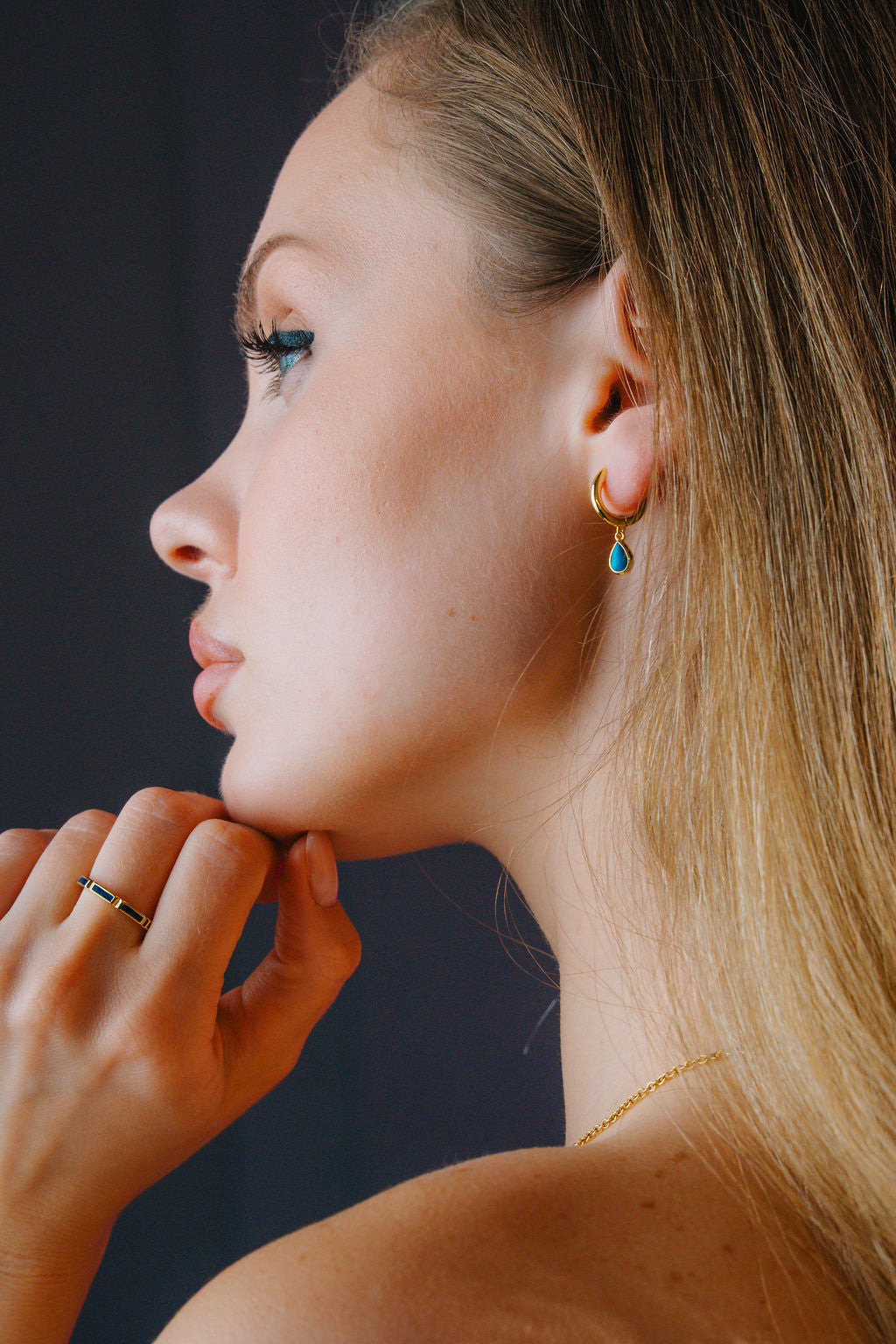 Close-up of a woman's profile with a  gold Turquoise huggee hoop earringdark background