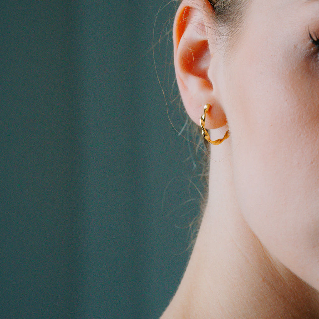 Close-up of a person wearing Twisted Rope Large Hoop earring against a teal background
