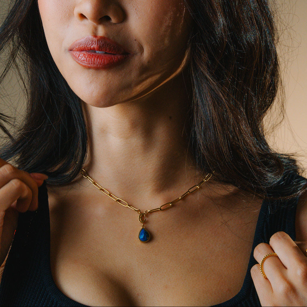 Close-up of a woman wearing a gold lapis lazuli necklace with a blue pendant.