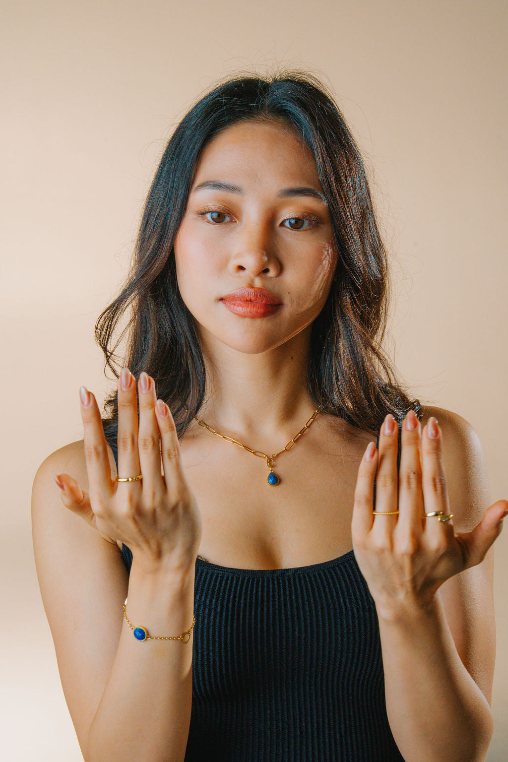 Woman wearing a gold lapiz lazuli necklace and bracelet jewelry against a beige background