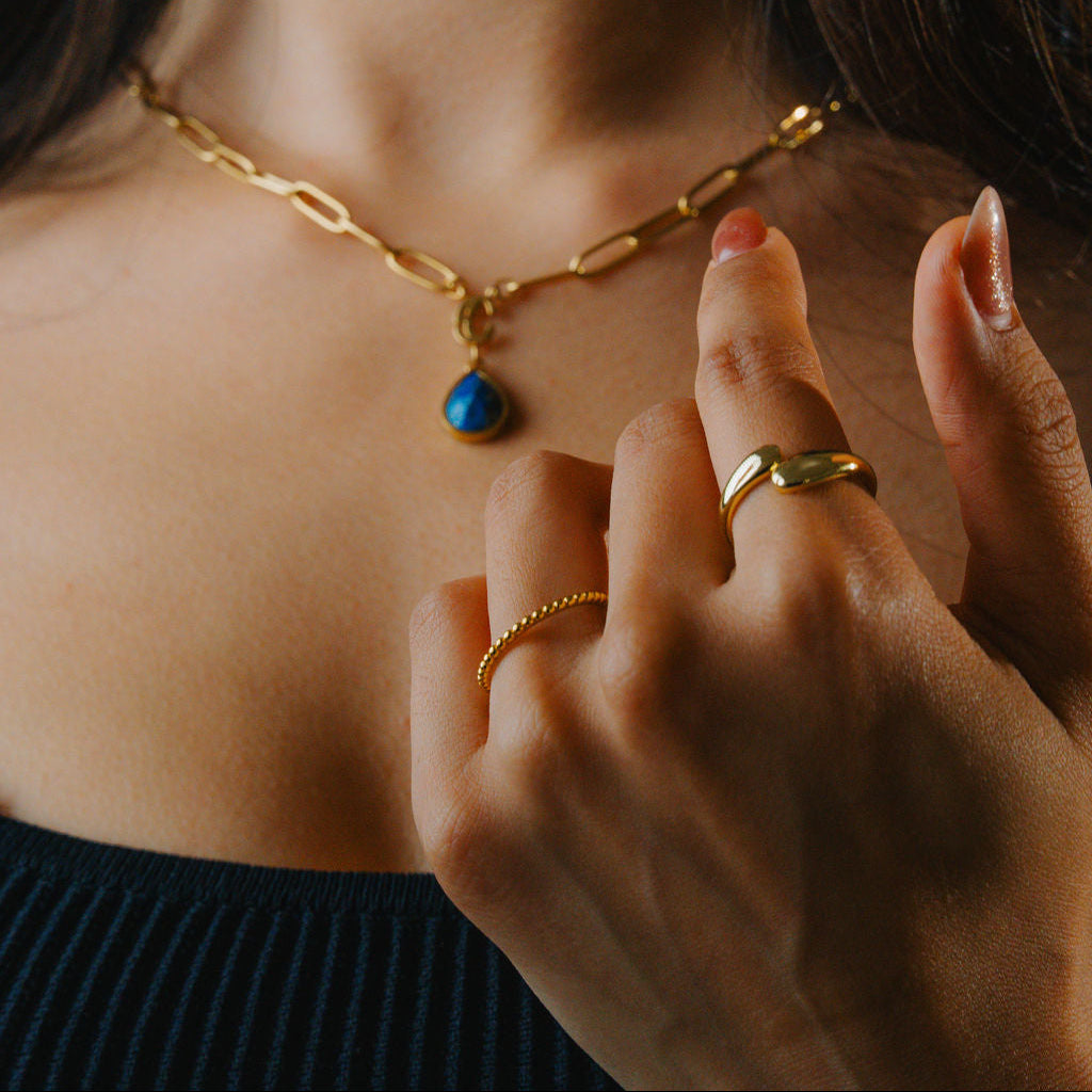 Close-up of a person wearing a Gold beaded ring, band stackable gold jewelry with a blue pendant.