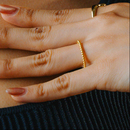 Close-up of a hand wearing a Gold beaded ring, band stackable on a textured black fabric background
