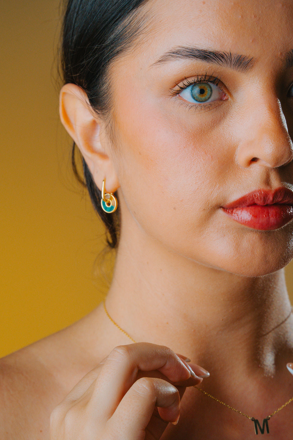 Close-up of a woman wearing gold earrings with a green Malachite and brown tiger eye stone hoop & the yellow background
