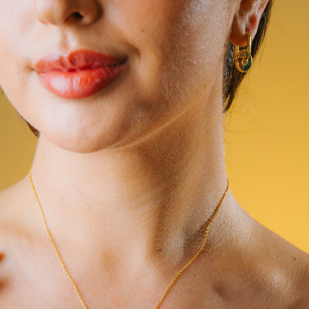 Close-up of a person wearing a gold necklace with a yellow background and green Malachite and brown tiger eye stone hoop 
