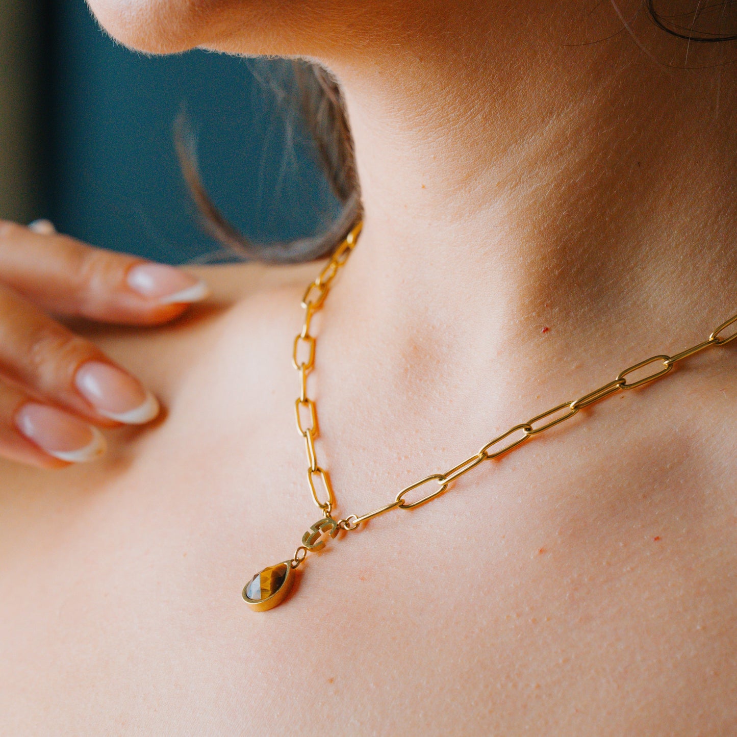 Close-up of a person wearing a gold tiger eye chain necklace with a pendant.