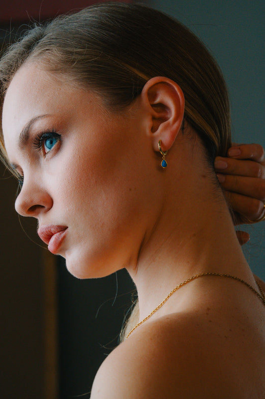 Close-up of a woman adjusting her gold  Turquoise huggee hoop earring with a blurred background 