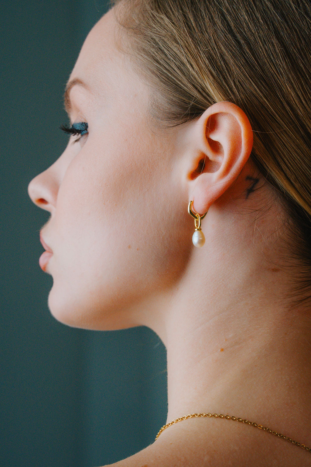Close-up of a person wearing  gold earring with a pearl detail against a dark background
